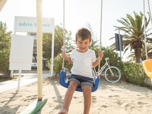 Bambino felice su un'altalena in spiaggia, vicino a una bicicletta.